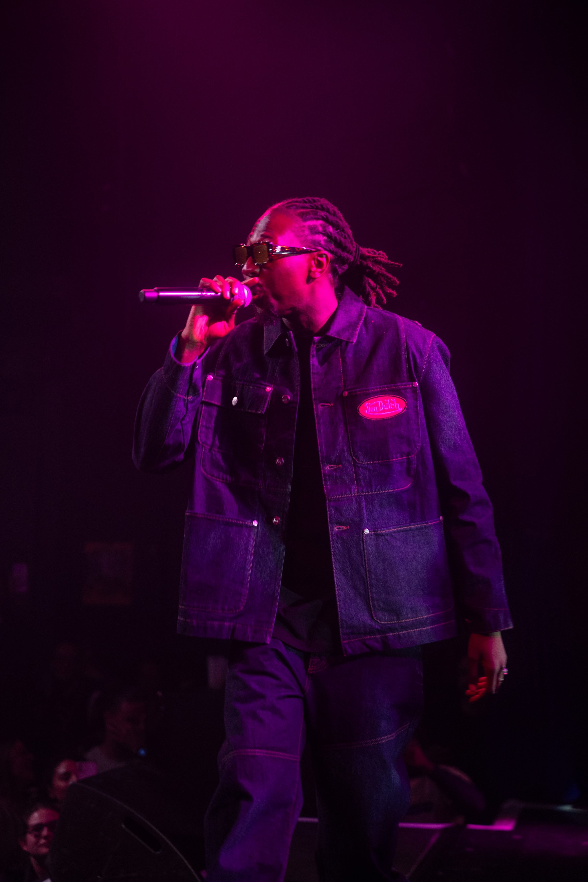 Le rappeur en veste de jean chante au micro dans une lumière violette