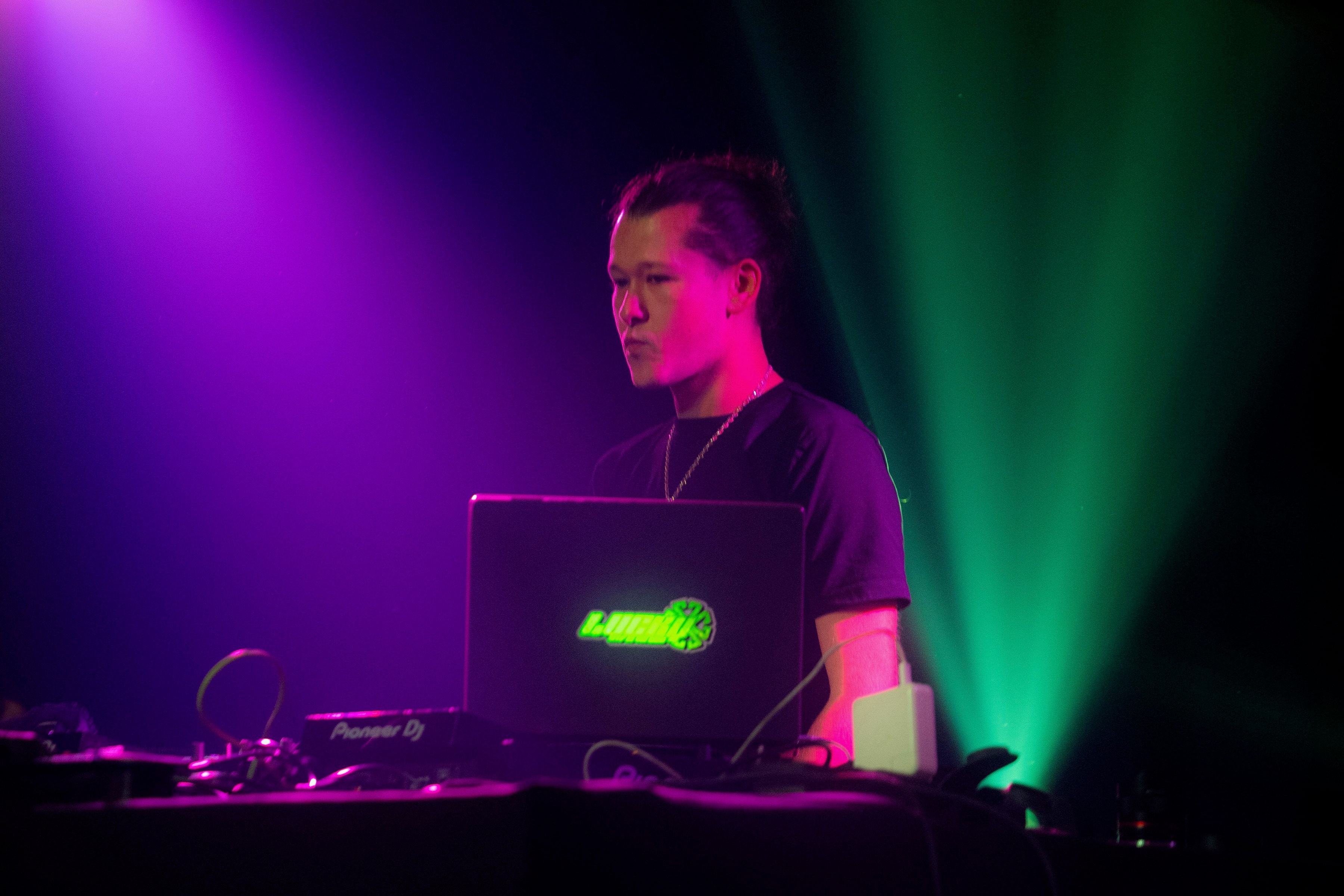 Le DJ penché sur son ordinateur, entre un faisceau violet et un faisceau vert