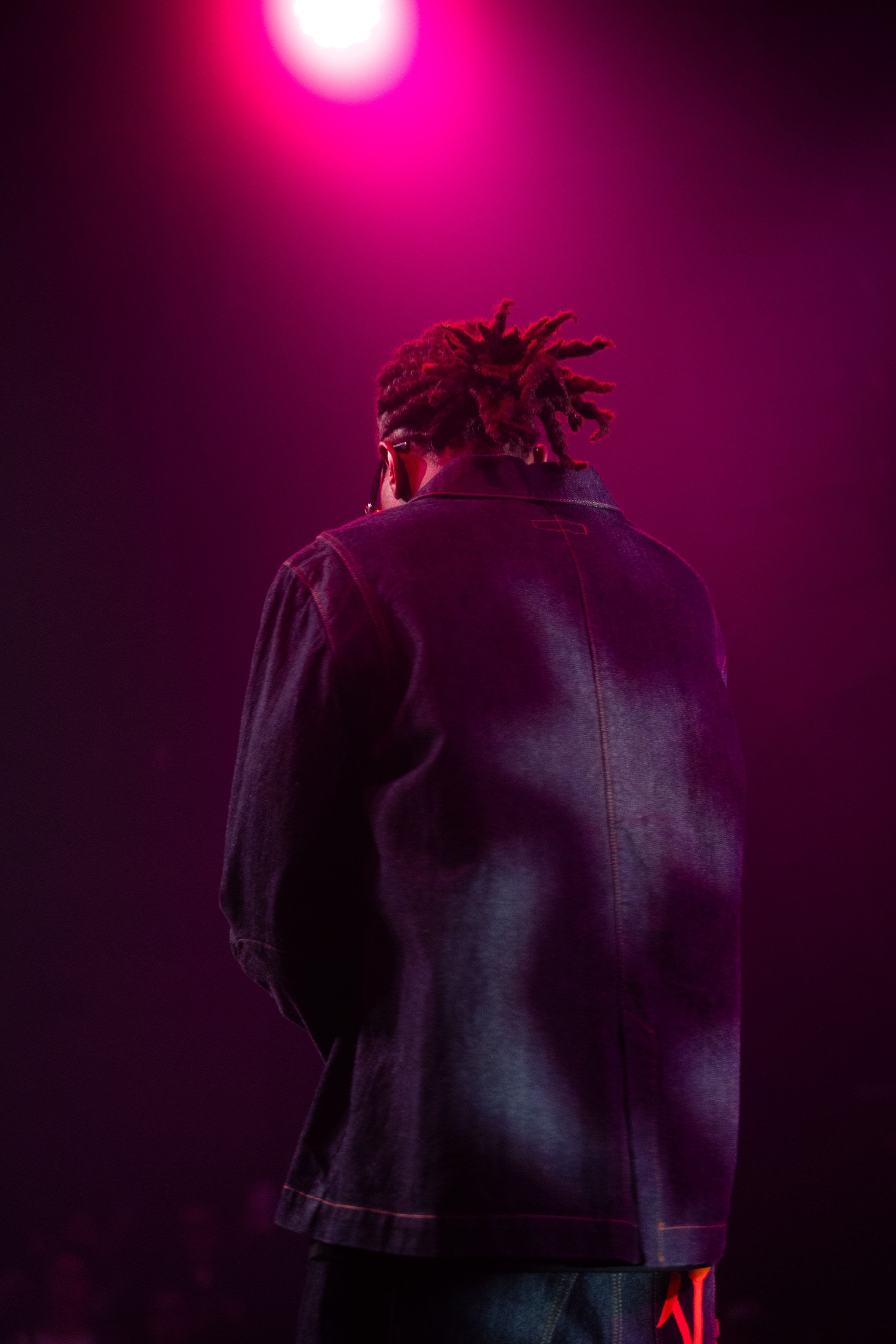 Le rappeur de dos, dreadlocks relevées, dans une lumière magenta