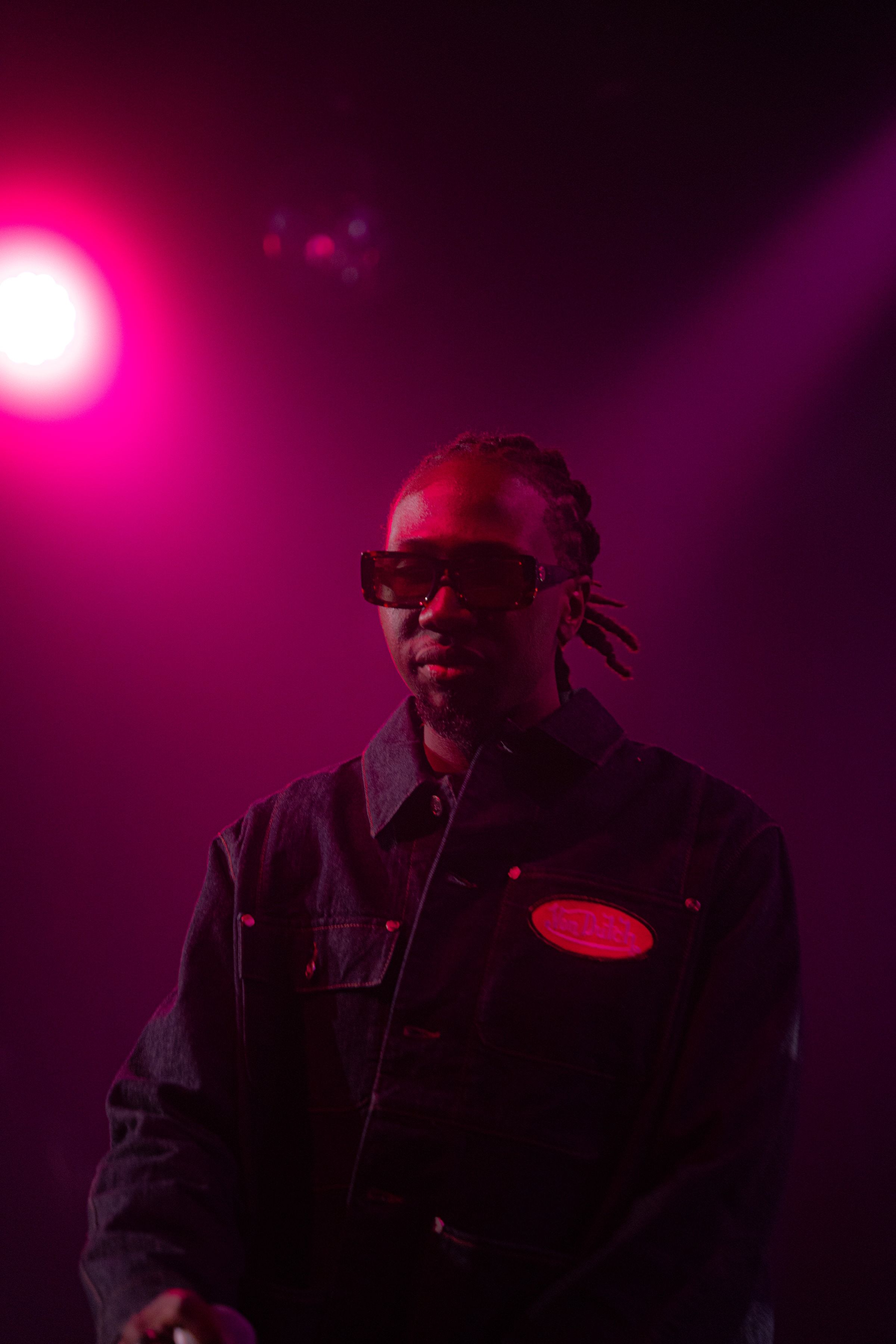 Le rappeur en lunettes noires, de face, sous un projecteur rose