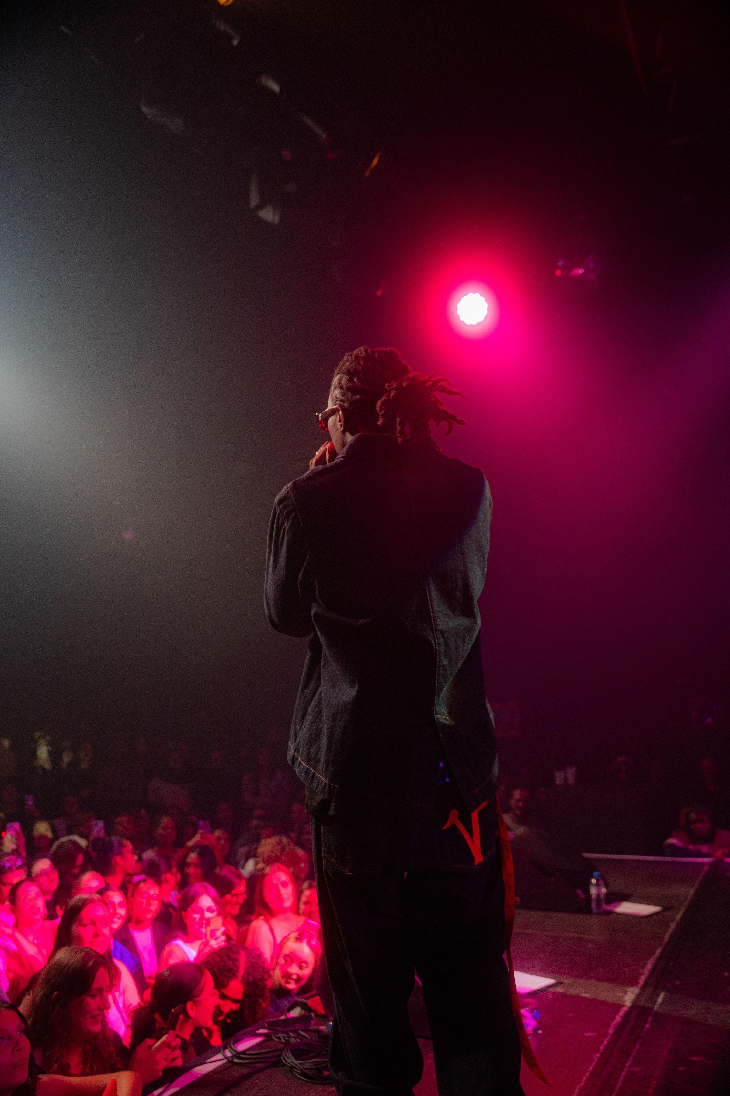 Le rappeur de dos au bord de la scène, la foule éclairée de rose en contrebas