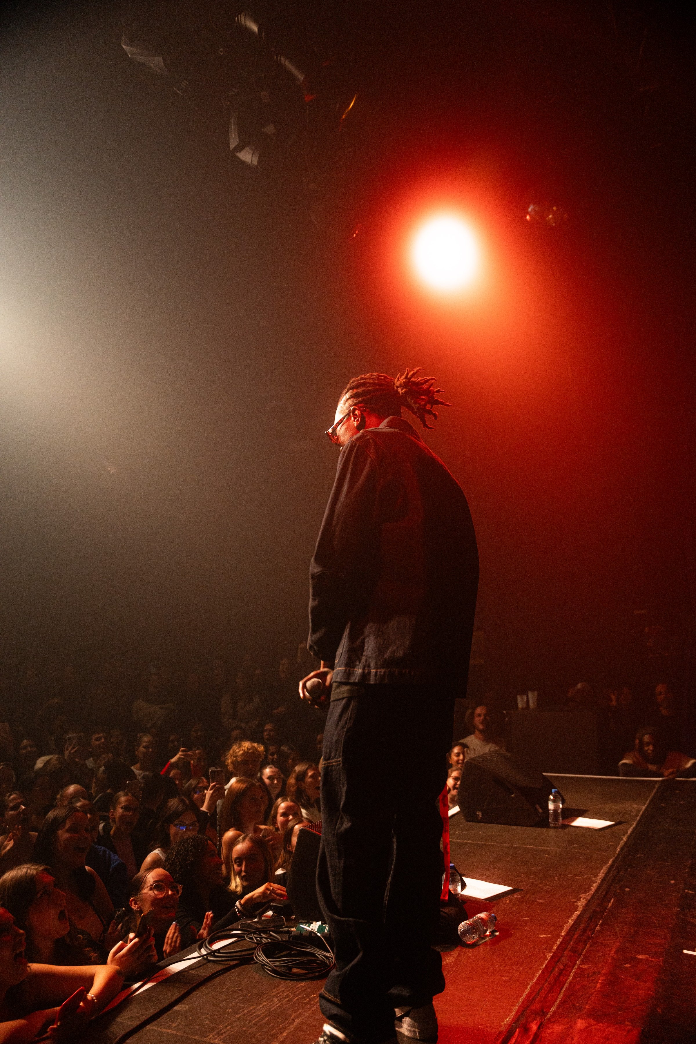 Le rappeur de dos sur scène face à la foule, sous un projecteur rouge