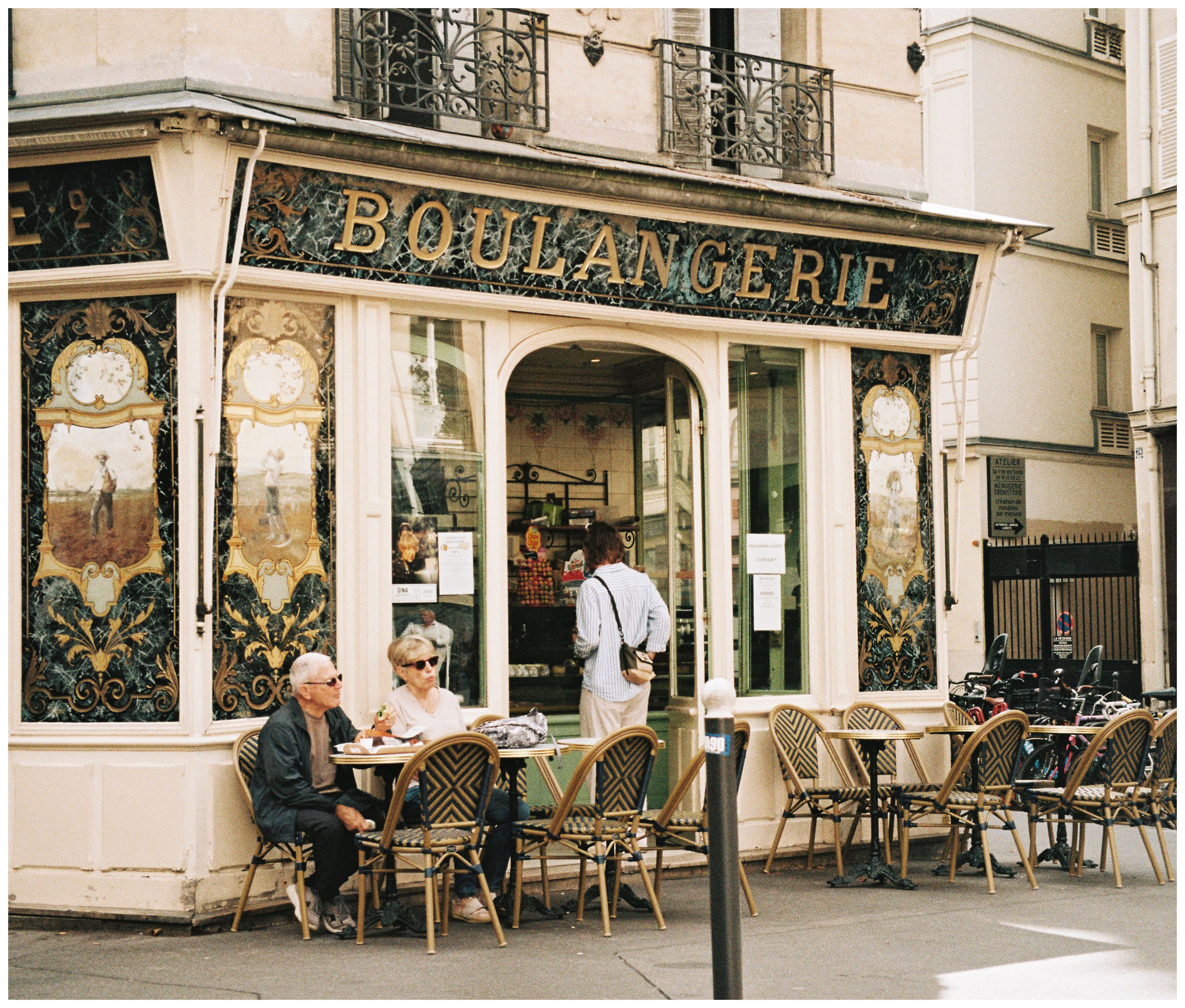 Façade d’une boulangerie ancienne aux panneaux peints, deux clients en terrasse