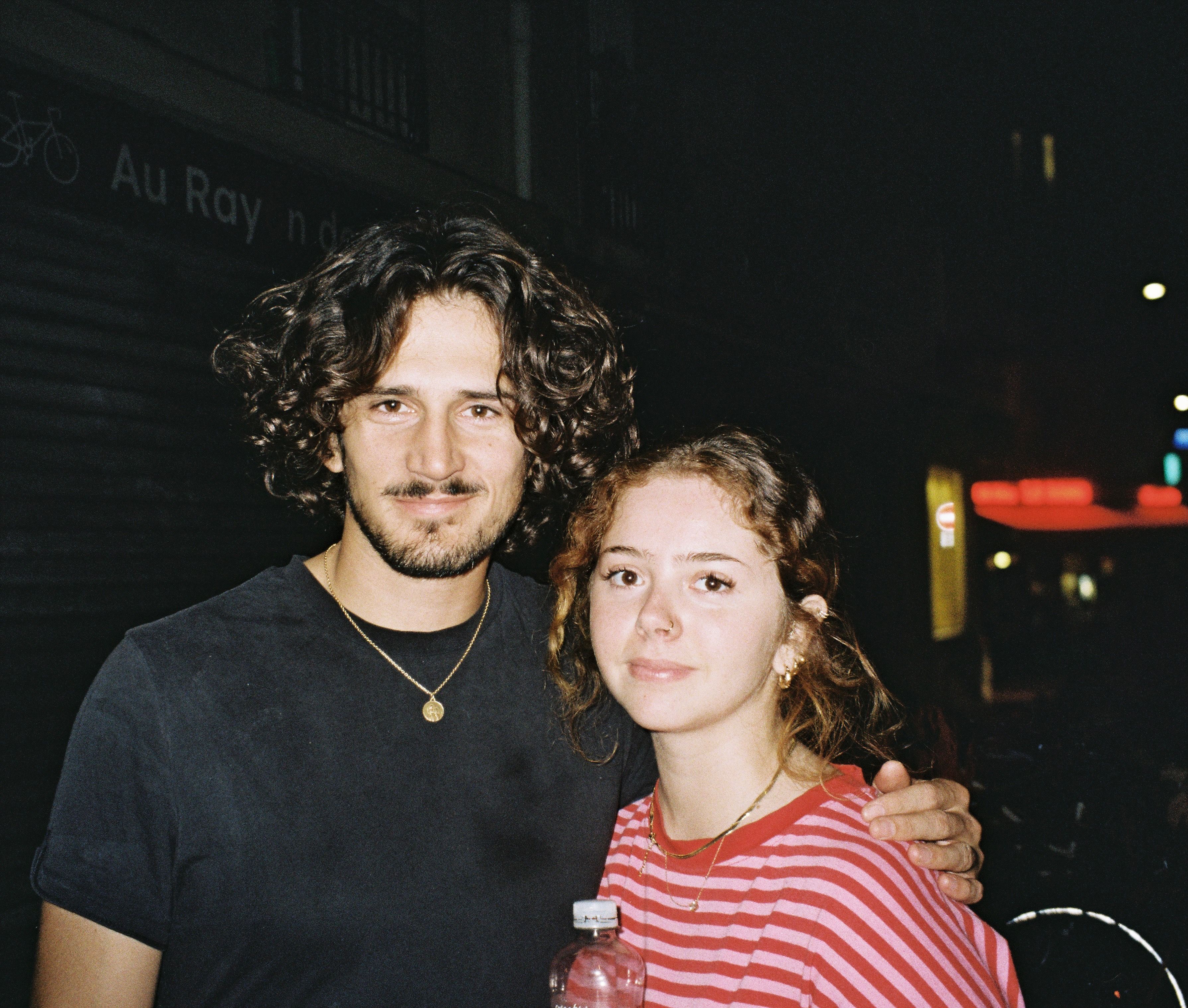 De nuit, un jeune homme aux cheveux bouclés pose avec une jeune fille en marinière rouge