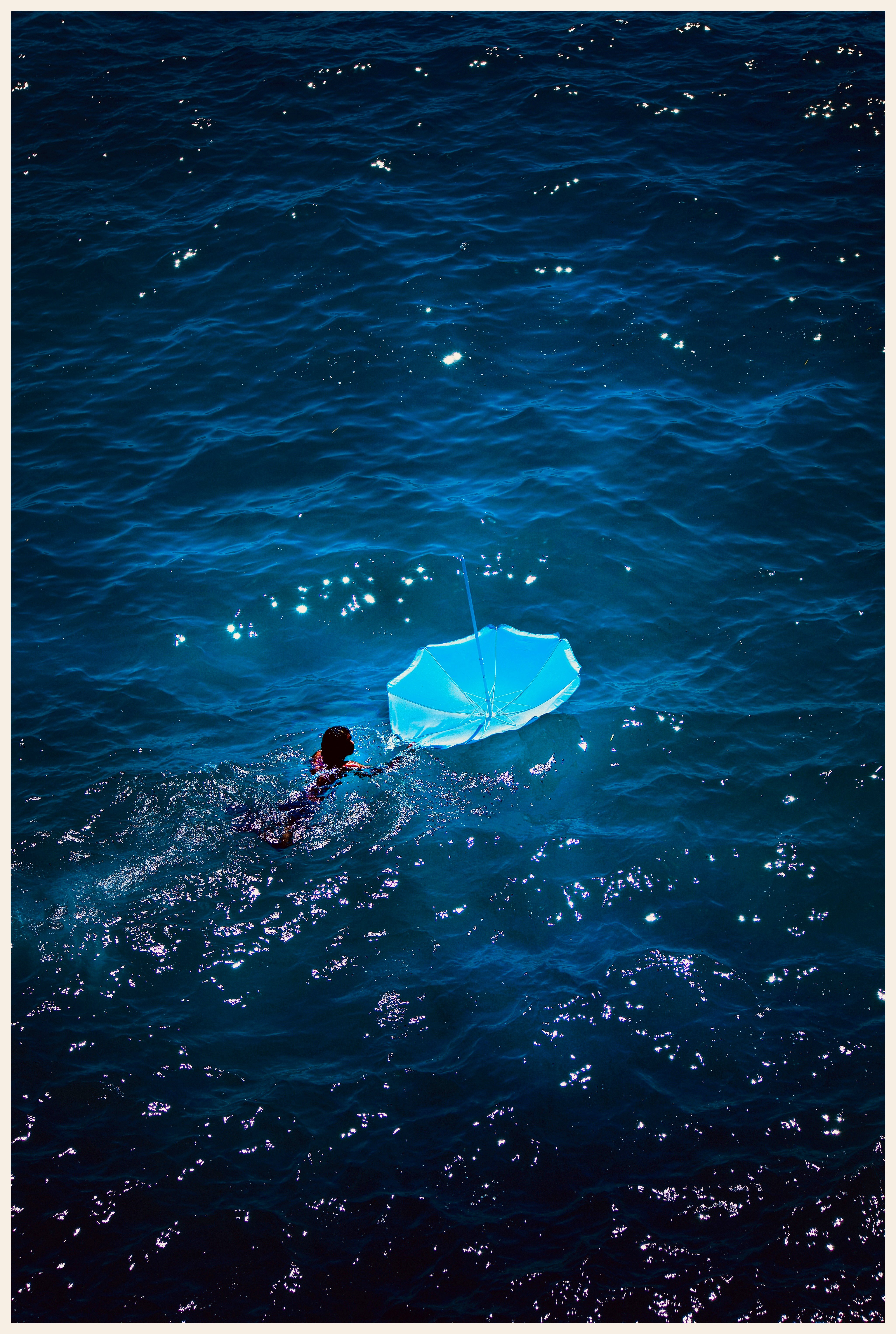 Un nageur tire un parasol bleu retourné sur une mer sombre et scintillante
